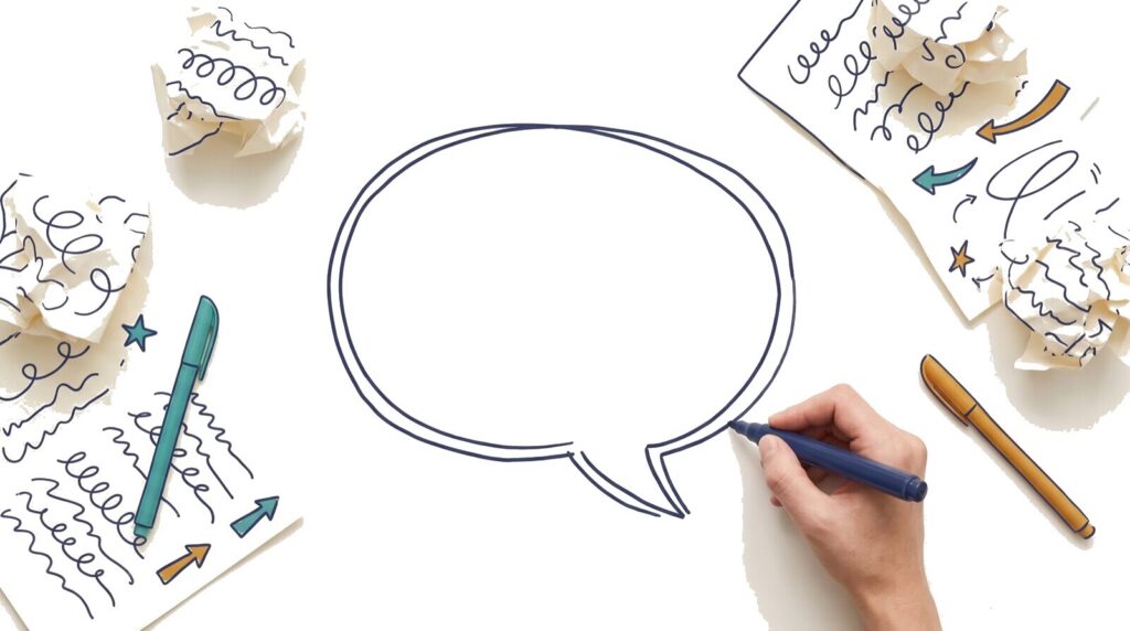 Hand drawing an empty speech bubble with a marker, crumpled draft pages scattered around