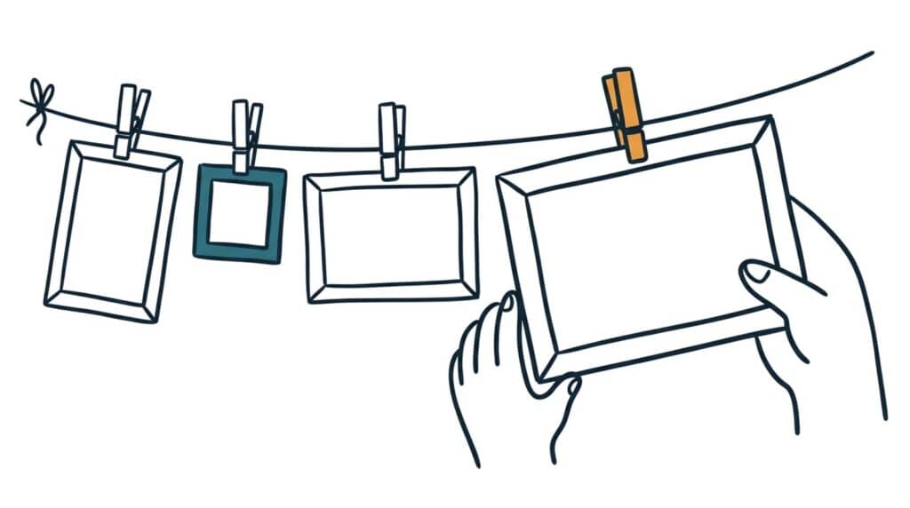 Marker doodle of empty picture frames in several sizes pegged to a washing line, a hand steadying the largest
